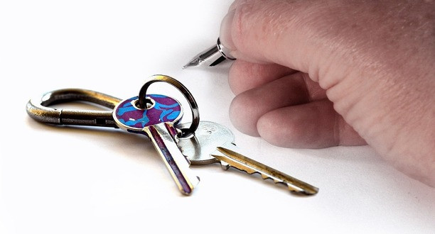 Schlüssel liegen auf weißem Untergrund. Eine Hand hält einen Füller.