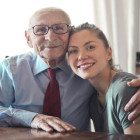 Alter Mann und junge Frau sitzen gemeinsam an einem Tisch und lächeln.