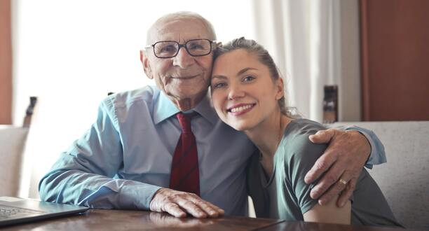 Alter Mann und junge Frau sitzen gemeinsam an einem Tisch und lächeln.