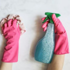 Zwei Hände mit pinken Handschuhen. Die linke hält einen Putzlappen, die rechte Reinigungsmittel.