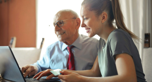 Alter Mann mit junger Frau an einem Laptop.