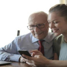 Enkelin sitzt neben ihrem Opa und zeigt ihm, wie ein Handy funktioniert.