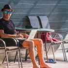 Mann sitzt mit Urlaubsoutfit auf einem Sonnenstuhl und hält Laptop auf dem Schoß.