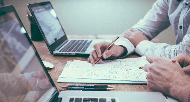 High angle view of businessmen hands touching white papers arranged on a rustic wooden table forming a yellow light bulb. Conceptual for bright business ideas and innovations.