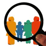 Schematisch abgebildete Menschen unter einer Lupe.