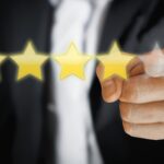 Das Bild zeigt eine Hand, die auf eine 5-Sterne-Skala zeigt, wobei vier Sterne leuchten und der fünfte angedeutet ist. Es handelt sich um ein symbolisches Motiv für Themen wie Kundenzufriedenheit, Online-Reputation und Feedback-Management.