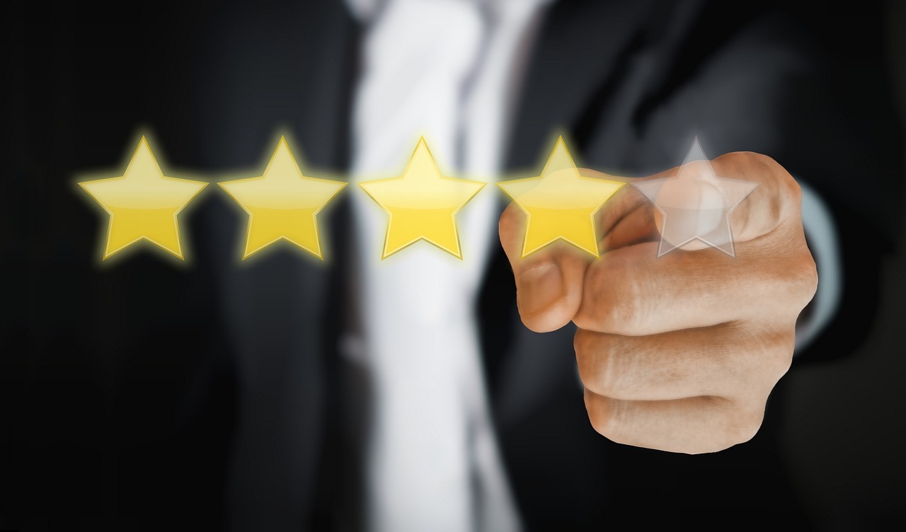 Das Bild zeigt eine Hand, die auf eine 5-Sterne-Skala zeigt, wobei vier Sterne leuchten und der fünfte angedeutet ist. Es handelt sich um ein symbolisches Motiv für Themen wie Kundenzufriedenheit, Online-Reputation und Feedback-Management.