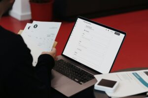 Eine Person sitzt mit einem Laptop und Papieren an einem Schreibtisch.