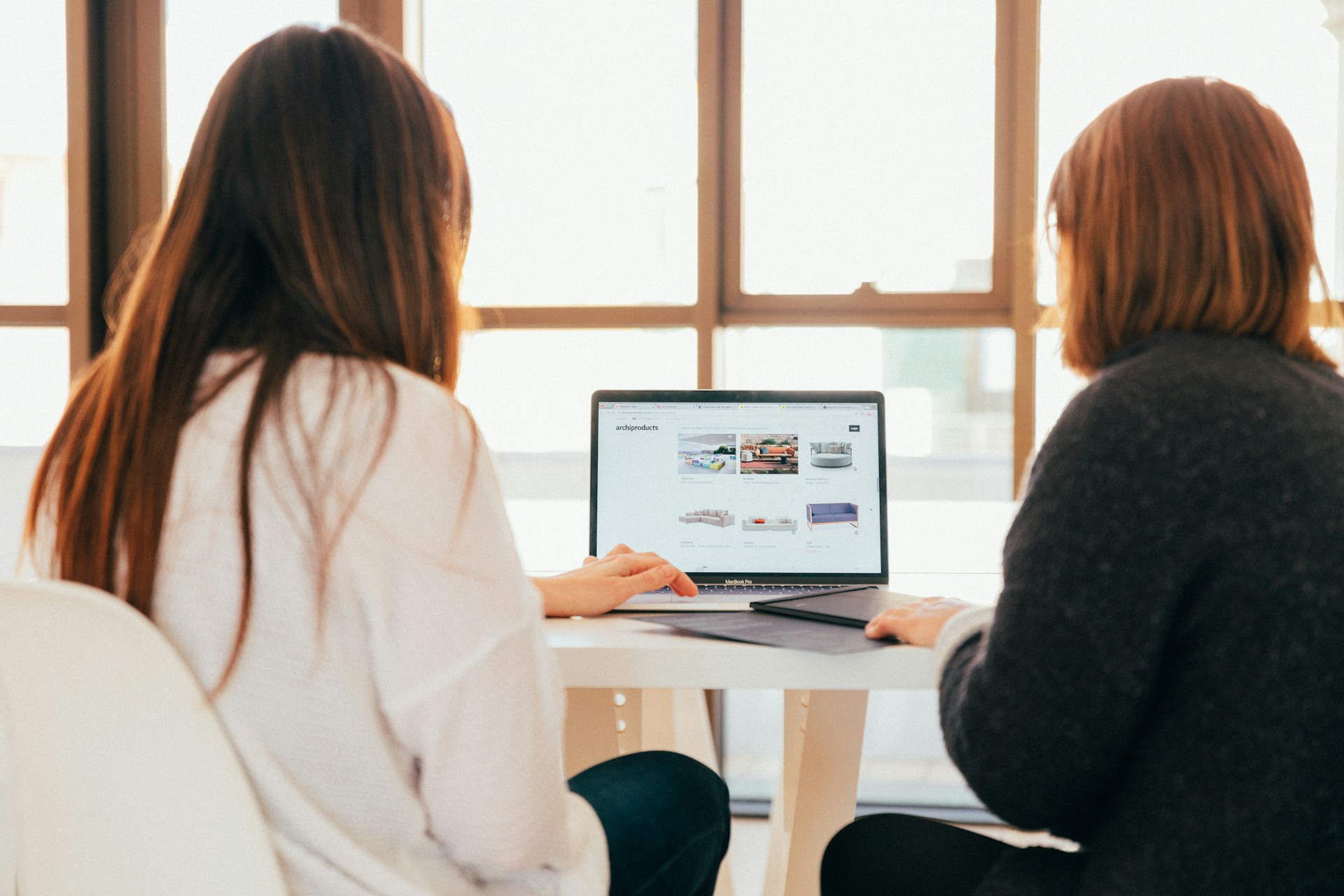 Zwei Frauen sitzen an einem Laptop, auf dem Display ist ein Onlineshop sichtbar.