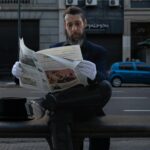 Mann liest Zeitung auf Parkbank.