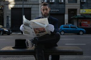 Mann liest Zeitung auf Parkbank.