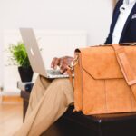 Mann mit Ledertasche hat einen Laptop auf dem Schoß.