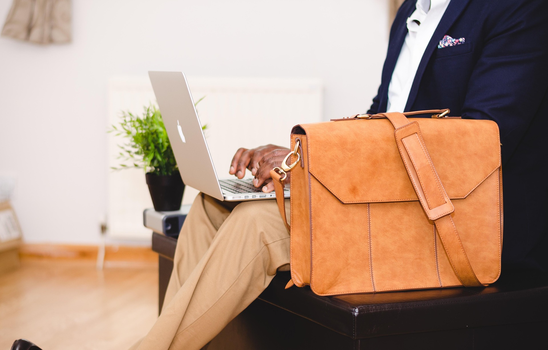 Mann mit Ledertasche hat einen Laptop auf dem Schoß.